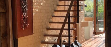 A staircase with wooden steps and metal railings, leading to a room with a brick wall and a hanging decorative piece.