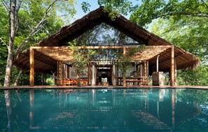 Une structure en bois avec un toit de chaume, une piscine et une vue sur les arbres environnants.