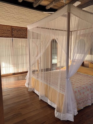 A room with a four-poster canopy bed, wooden flooring, and a brick wall.
