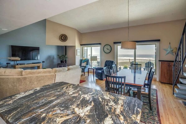 A spacious living area with a large sofa, a dining table with chairs, a TV, and a staircase leading to an upper level. - Gearhart House G740 (Gearhart)