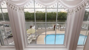 Vue depuis une chambre dotée de grandes fenêtres donnant sur un espace piscine, comprenant une piscine et un coin salon extérieur.