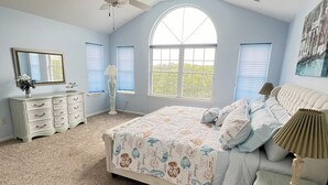 Une chambre à coucher avec un grand lit, une commode, une coiffeuse et un ventilateur de plafond.