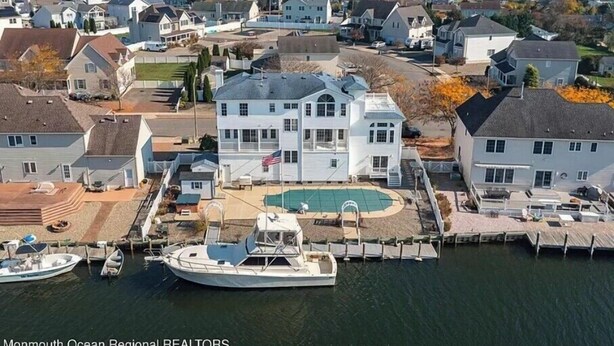 Un quartier résidentiel situé sur la côte, avec une grande maison blanche dotée d’une piscine et de plusieurs bateaux amarrés.
