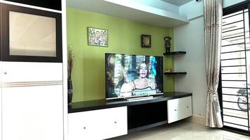 A living room with a TV on a white entertainment unit, green walls, and a window with a curtain.