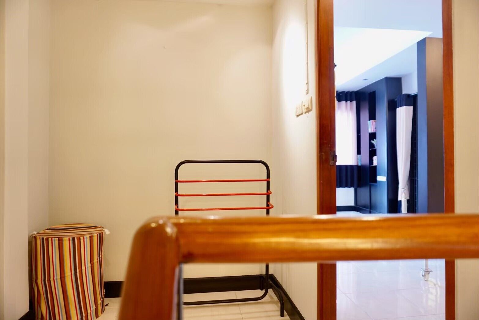 A narrow hallway with a wooden chair in the foreground, a striped ottoman, and a metal rack with red handles.