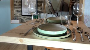 A dining area with a wooden table set for four, including plates, cutlery, and glasses. A hammock hangs from the ceiling, and a framed picture is on the wall.