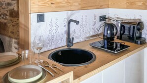 A wooden kitchen with a stone wall, a black sink, white cabinets, and a coffee machine.