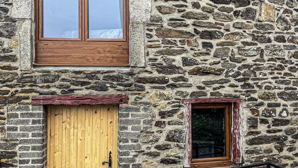 A stone building with a wooden door and window, a small window, and a metal railing.