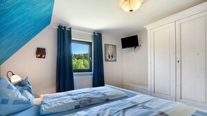 Un dormitorio con cama, cortinas, ventana, televisor y armario.