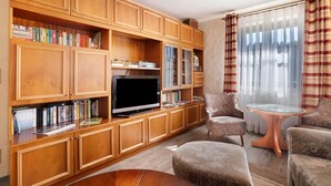 Una sala de estar con armarios de madera, un televisor, estanterías y dos sillones.