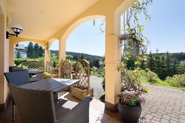 An outdoor patio with wicker furniture, a wooden table, and a potted plant.