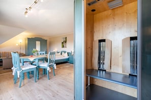 A room with a wooden ceiling, a bed with a headboard, a dining table with chairs, and a sofa in the background. - 'Superior Einraumappartement mit Infrarotkabine' (Marienberg)