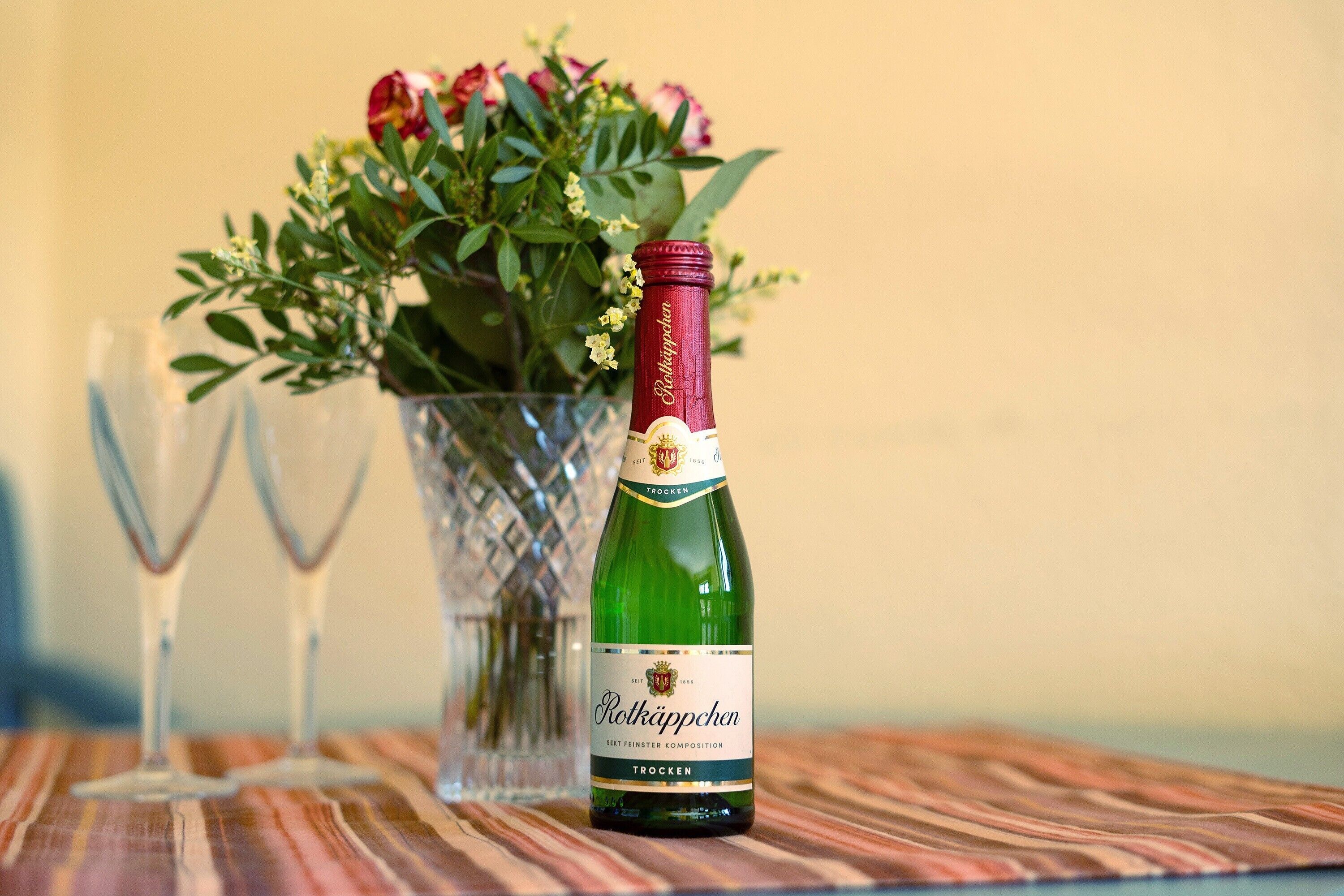 Une bouteille de vin Rothäppchen avec son étiquette, un verre et un vase rempli de fleurs, le tout posé sur une table.