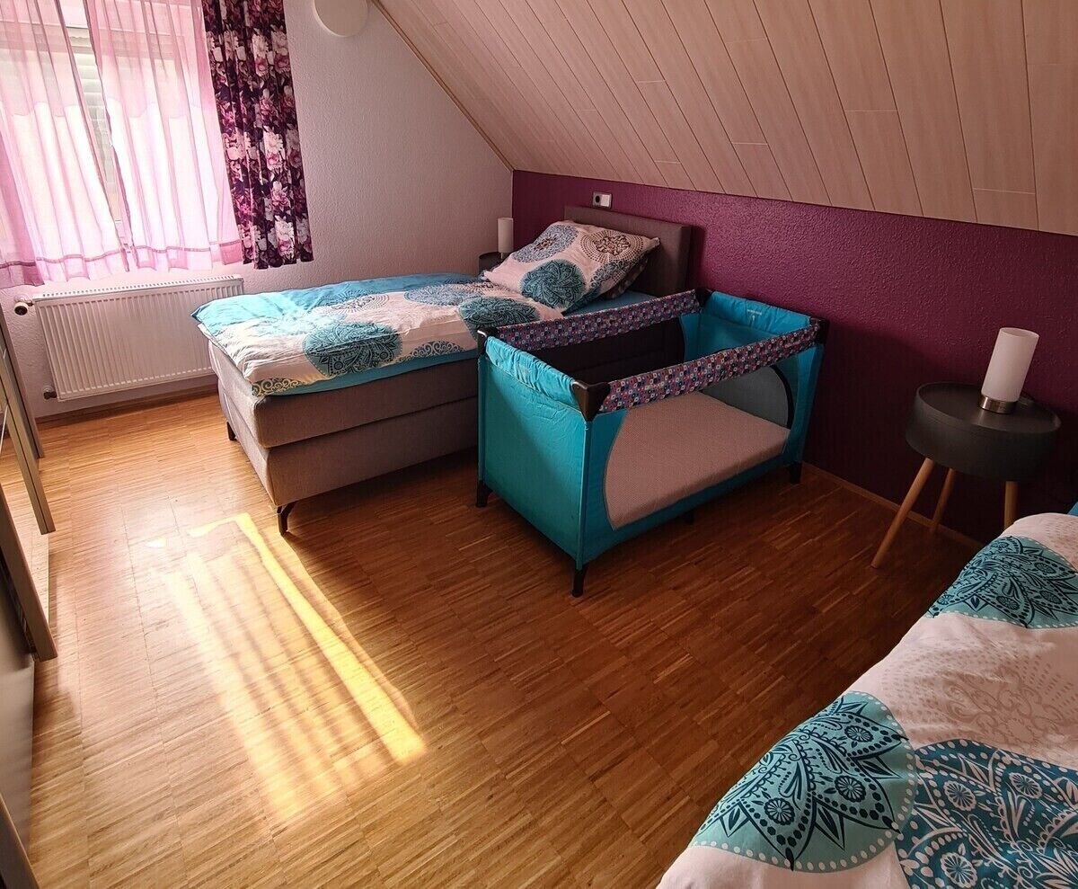 A bedroom with a bed, a small sofa, a window with curtains, a radiator, and a wooden floor.