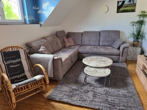 Una sala de estar con un sofá seccional gris, una mesa de centro de mármol redonda, una silla de mimbre y un tapete gris.