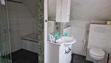 Een badkamer met een douche, wastafel, toilet en een spiegel boven de wastafel.