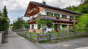 A traditional two-story building with a balcony, a wooden fence, and a paved pathway. - Apartment 'Ferienwohnung Regina' with Mountain View, Balcony and Wi-Fi (Mittenwald)