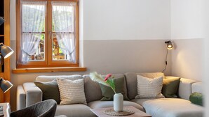 A living room with a sofa, pillows, a vase with flowers, a lamp, and a window with curtains. - Apartment 'Ferienwohnung Regina' with Mountain View, Balcony and Wi-Fi (Mittenwald)
