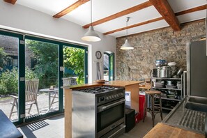 A kitchen with a gas stove, oven, and a stone wall.