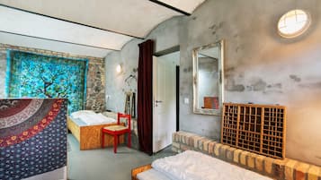 Un dormitorio con cama, una silla, un tapiz, un espejo y una pared de piedra.