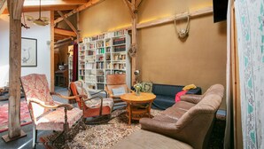 A cozy living room with a wooden ceiling, a bookshelf, a sofa, and a chair. - Finca 'Gruppenhaus' with Shared Terrace, Communal Garden and Wi-Fi (Groß Kreutz (Havel))