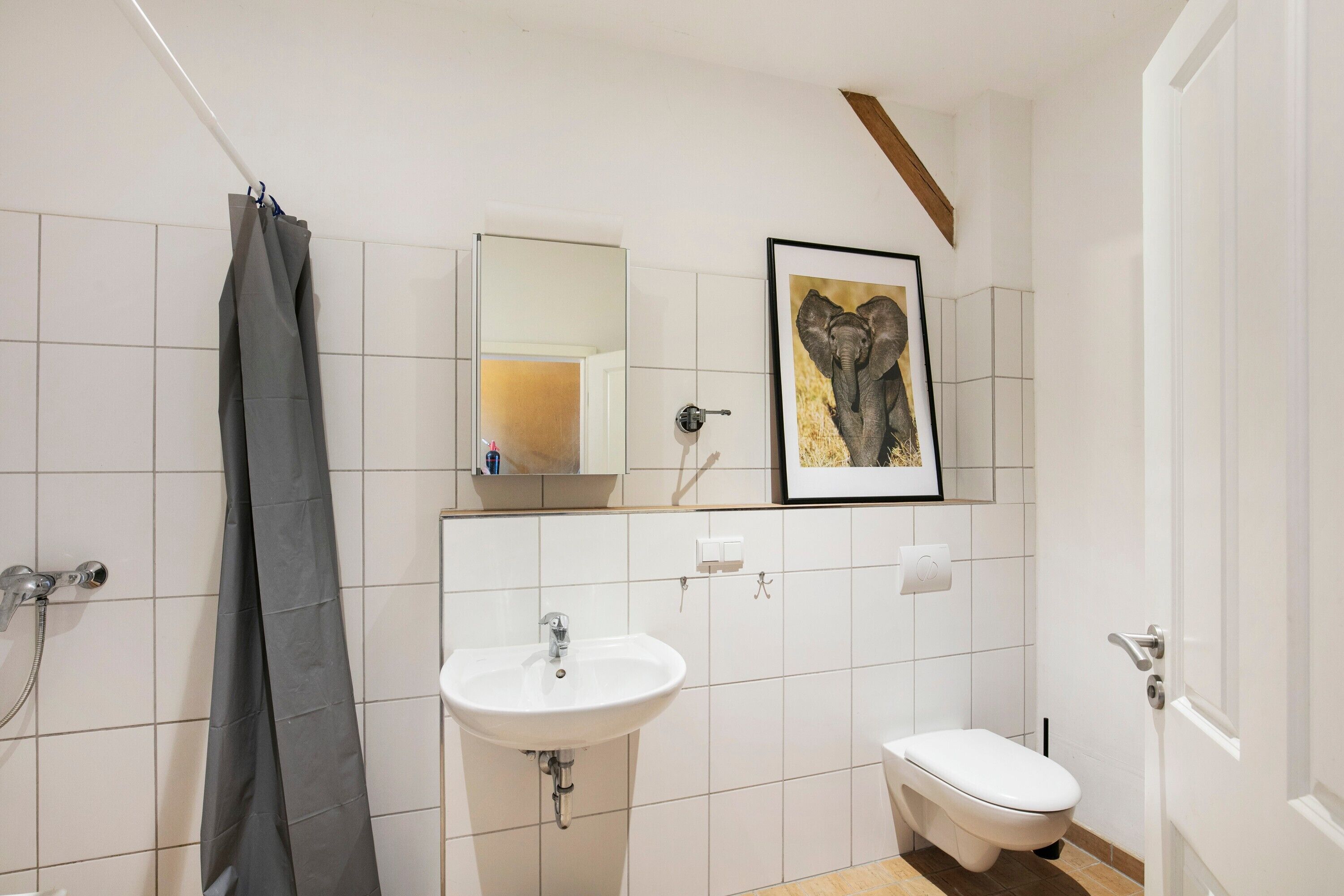 Ein Badezimmer mit Duschvorhang, Waschbecken, Toilette, einem gerahmten Bild und einem Spiegel.