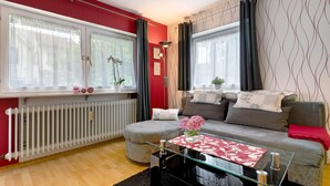 Un salon avec un canapé, une table basse en verre, un radiateur et une fenêtre avec des rideaux.