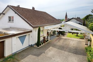 A house with a sloped roof, a covered driveway, and a small garden area with potted plants.
