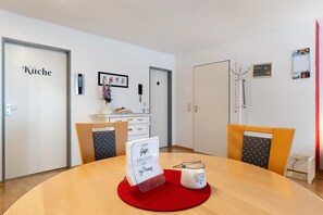 A hotel room with a wooden dining table, a red placemat, a framed sign, a small vase with flowers, and a white cabinet. - Apartment 'Villa Stumpf' with Mountain View, Private Terrace and Wi-Fi (Friesenheim)
