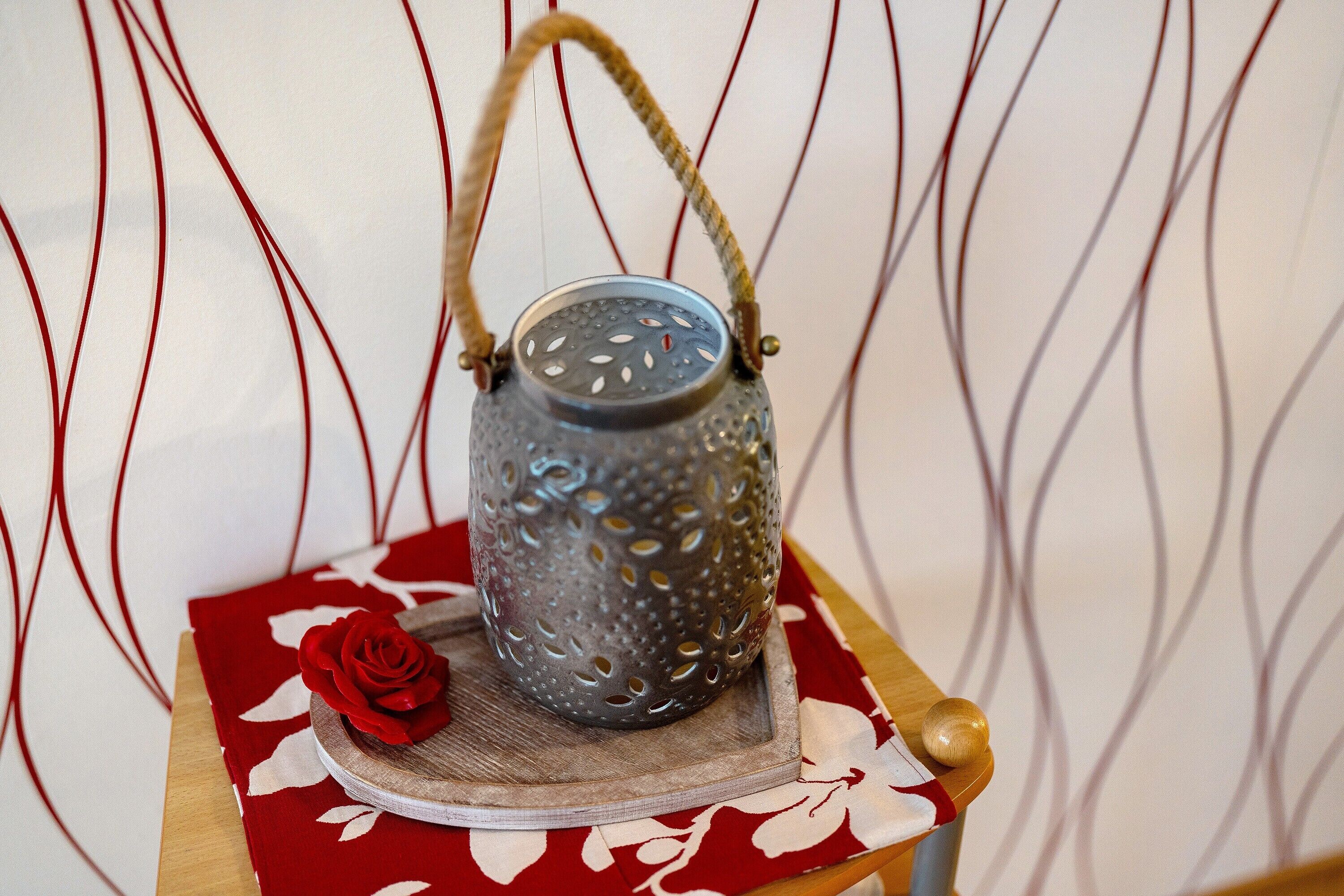A lantern with a textured surface and a handle, placed on a wooden surface with a red and white patterned cloth underneath.