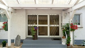 Une entrée d’immeuble avec un porche abrité, un escalier et des plantes en pot.
