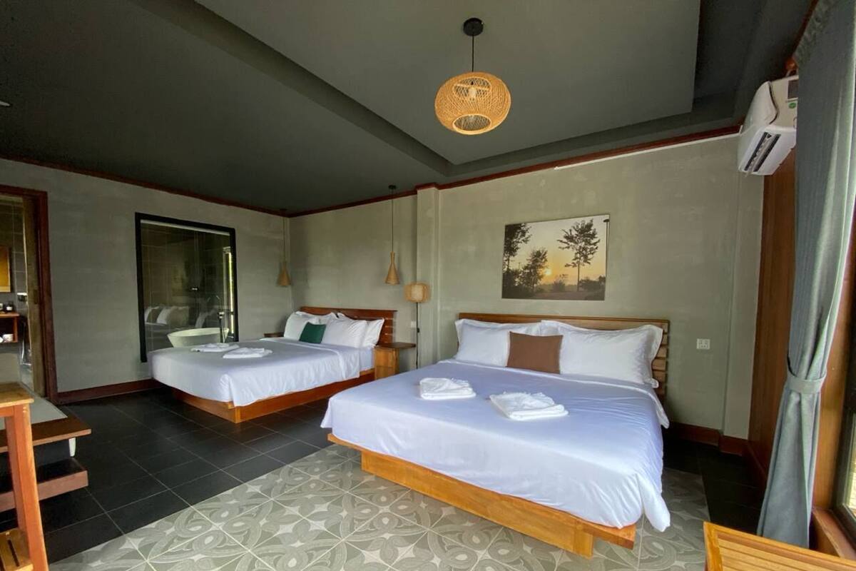 Una habitación de hotel con dos camas, un espejo grande, un cuadro y un ventilador de techo.