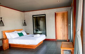 Un dormitorio con cama de madera, una mesita, un armario y un baño visible a través de una puerta de cristal.
