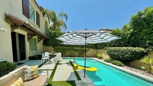 Una piscina amb tobogan, zona de relax amb coixins i una parasol de terrassa.