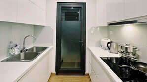 A compact kitchen with white cabinets, a stainless steel sink, a black door, and a stove with pots and pans. - NVT Housing - Vinhomes Skylake Apartment (Hanoi)