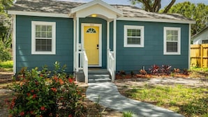 A single-story house with a front porch, a yellow door, and a mailbox.