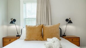 A neatly made bed with two pillows, a white towel, and two bedside tables with lamps.