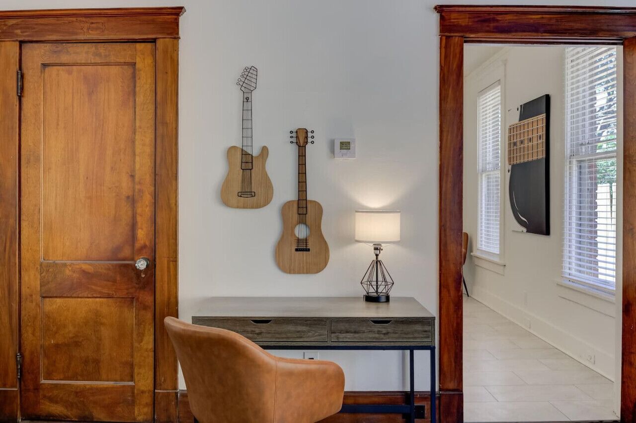 A room with a wooden door, a desk with a lamp, and two guitars on the wall.