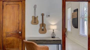A room with a wooden door, a desk with a lamp, and two guitars on the wall.