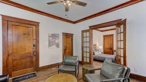 A room with wooden floors, a ceiling fan, a sofa, a chair, a small round table, and a door leading to another room. - The Cooper Suite | Midtown Memphis (Memphis)