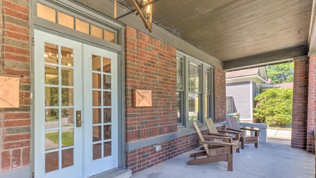 A covered patio with a brick wall, large sliding glass doors, and wooden chairs. - The Cooper Suite | Midtown Memphis (Memphis)