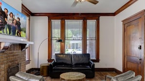A living room with a black leather sofa, two armchairs, a coffee table, a fireplace, and a large window with blinds. - The Cooper Suite | Midtown Memphis (Memphis)