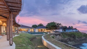 Una propiedad costera con un camino curvo que lleva a una casa con un amplio ventanal, una piscina y vistas al océano.