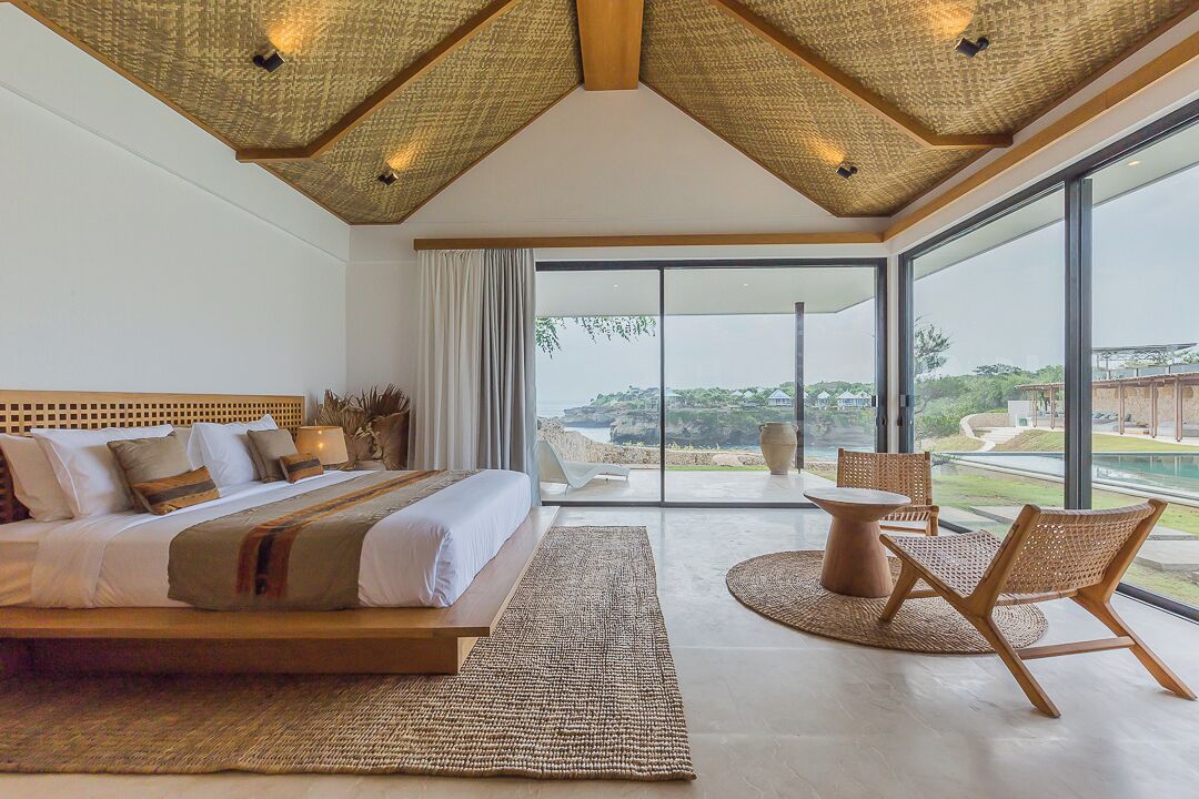 A spacious bedroom with a large bed, a view of the outdoors, and a balcony with seating.