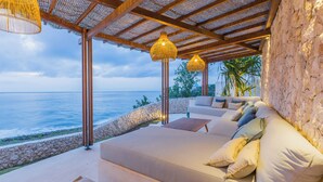 Un salón junto al mar con zona de estar acolchada, pared de piedra y vista al océano.