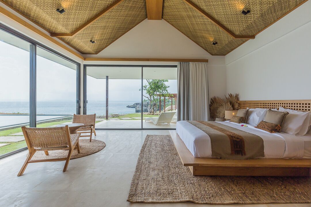 Een ruime slaapkamer met een groot bed, uitzicht op zee en een balkon met zitplaatsen buiten.