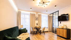 Un salon moderne avec un canapé vert, une table à manger avec des chaises, un meuble en bois et un téléviseur fixé au mur.