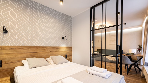 Une chambre d’hôtel avec un grand lit, une tête de lit en bois, un mur orné d’un motif géométrique, une porte coulissante et une petite table avec une chaise.