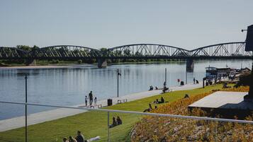 A riverside walkway with a bridge in the background, benches, and people relaxing.