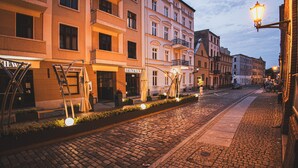 Une rue pavée bordée d’immeubles à plusieurs étages, dont certains arborent des enseignes bien visibles.